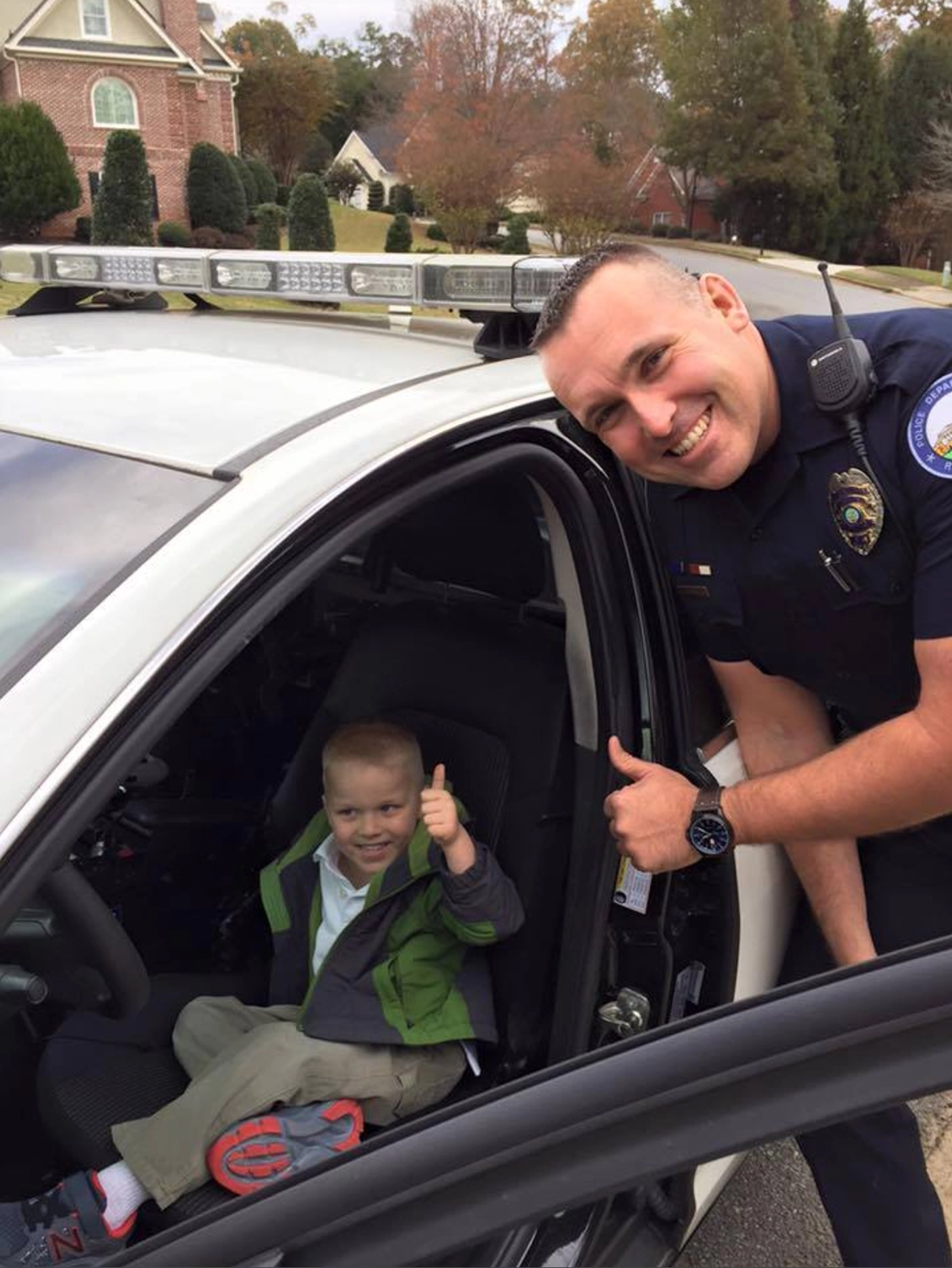 Roswell Police Officer Frechen smiling with a young boy giving thumbs up while sitting in a police cruiser