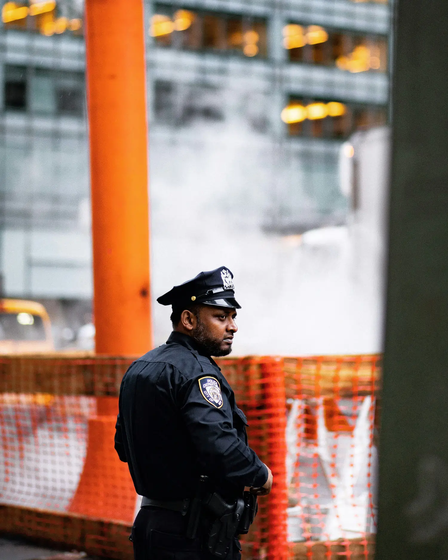 Police officer standing watch in an urban setting with city buildings in the background