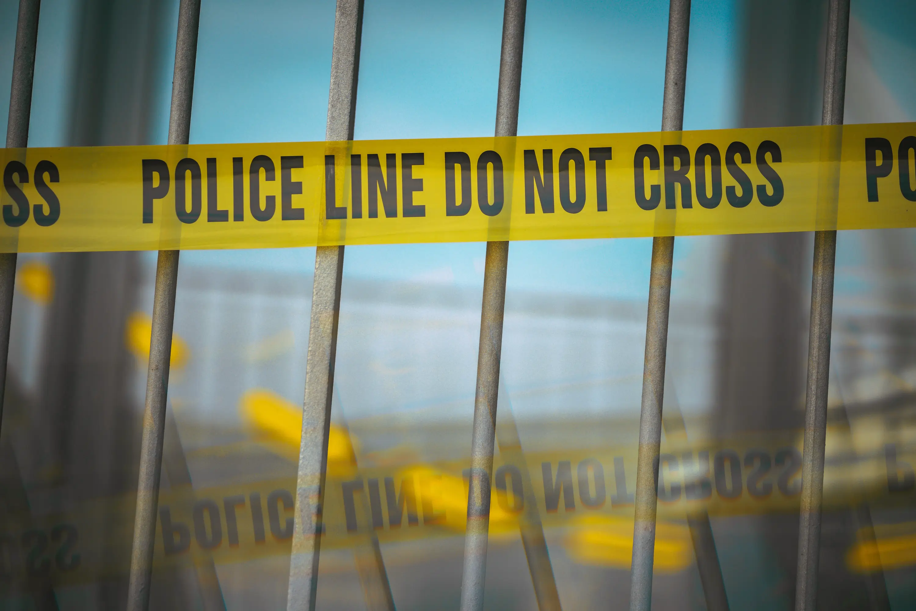 Yellow police tape reading 'POLICE LINE DO NOT CROSS' stretched across metal barriers