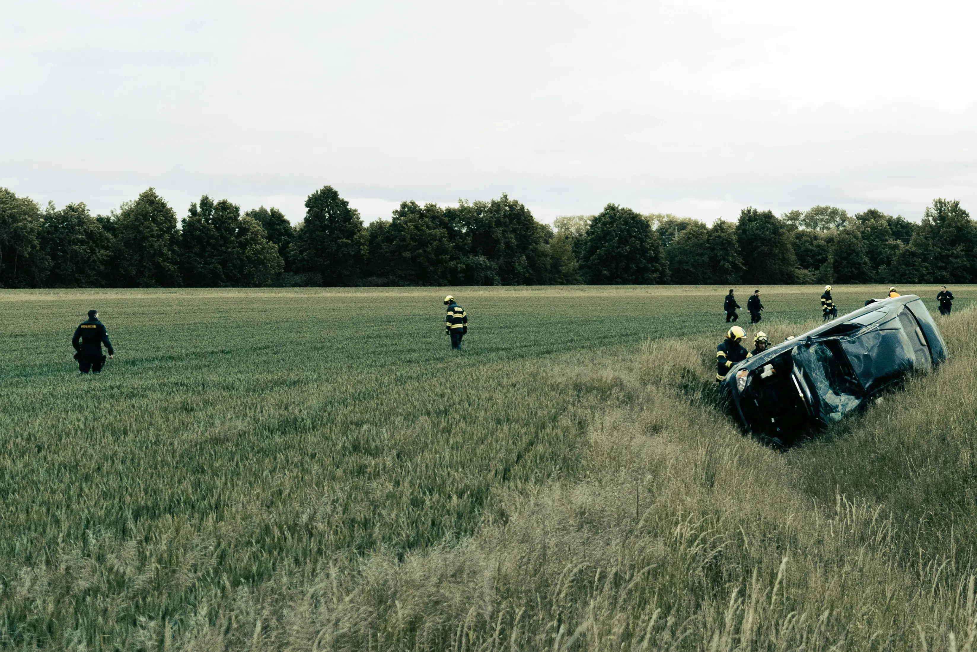 Overturned vehicle in a field with emergency responders walking across the scene